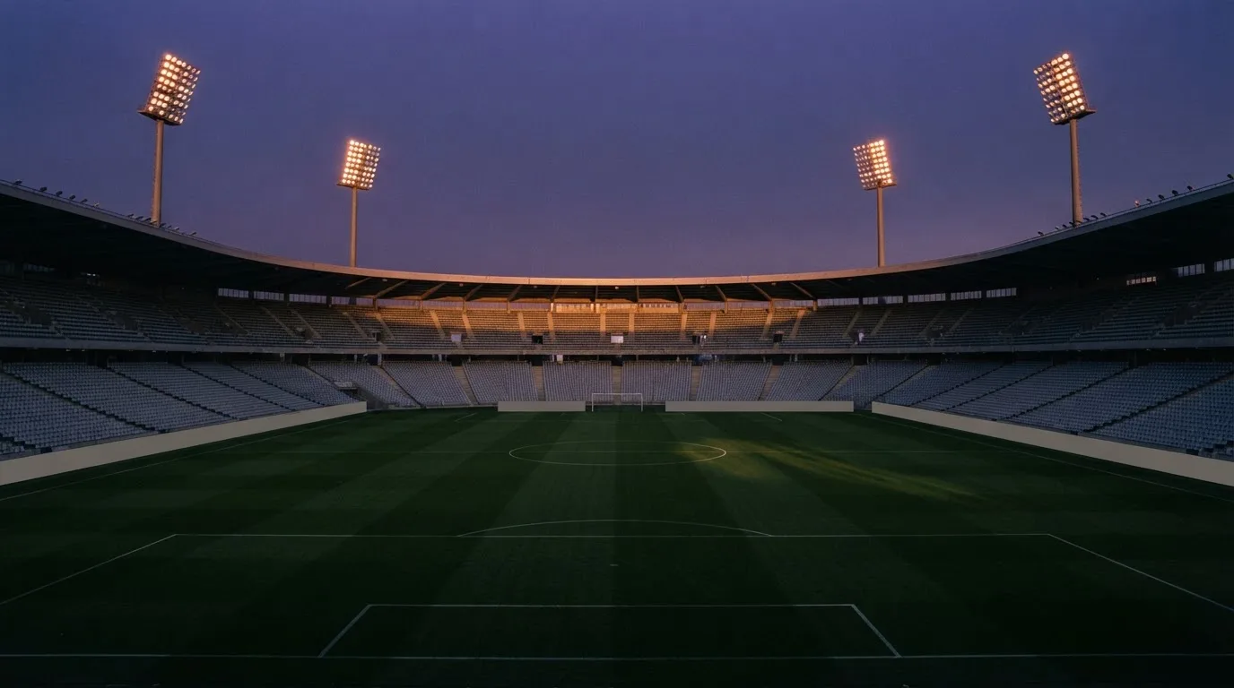 An empty football stadium with floodlight masts at dusk